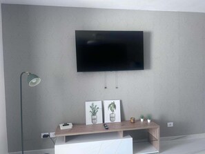 Un salon moderne avec un téléviseur fixé au mur, un bureau avec une lampe et deux œuvres d’art encadrées.