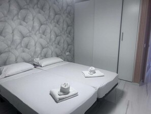 A hotel room with a large bed, two pillows, a headboard with a textured pattern, and a wardrobe.