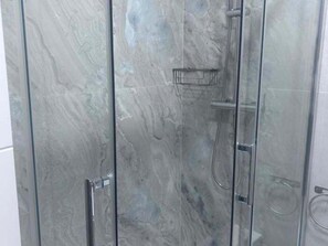 A bathroom with a glass shower enclosure and a marble wall.