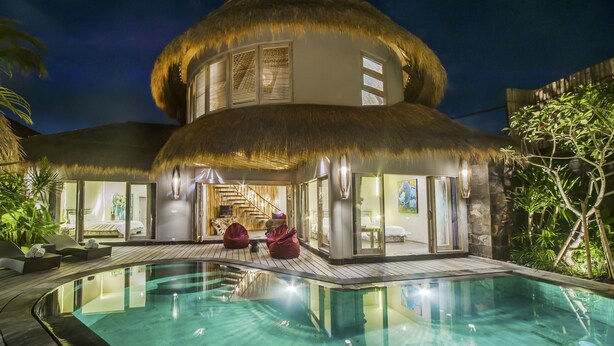 Un bâtiment à toit de chaume doté d’une piscine, de portes vitrées et d’un escalier menant à une chambre.