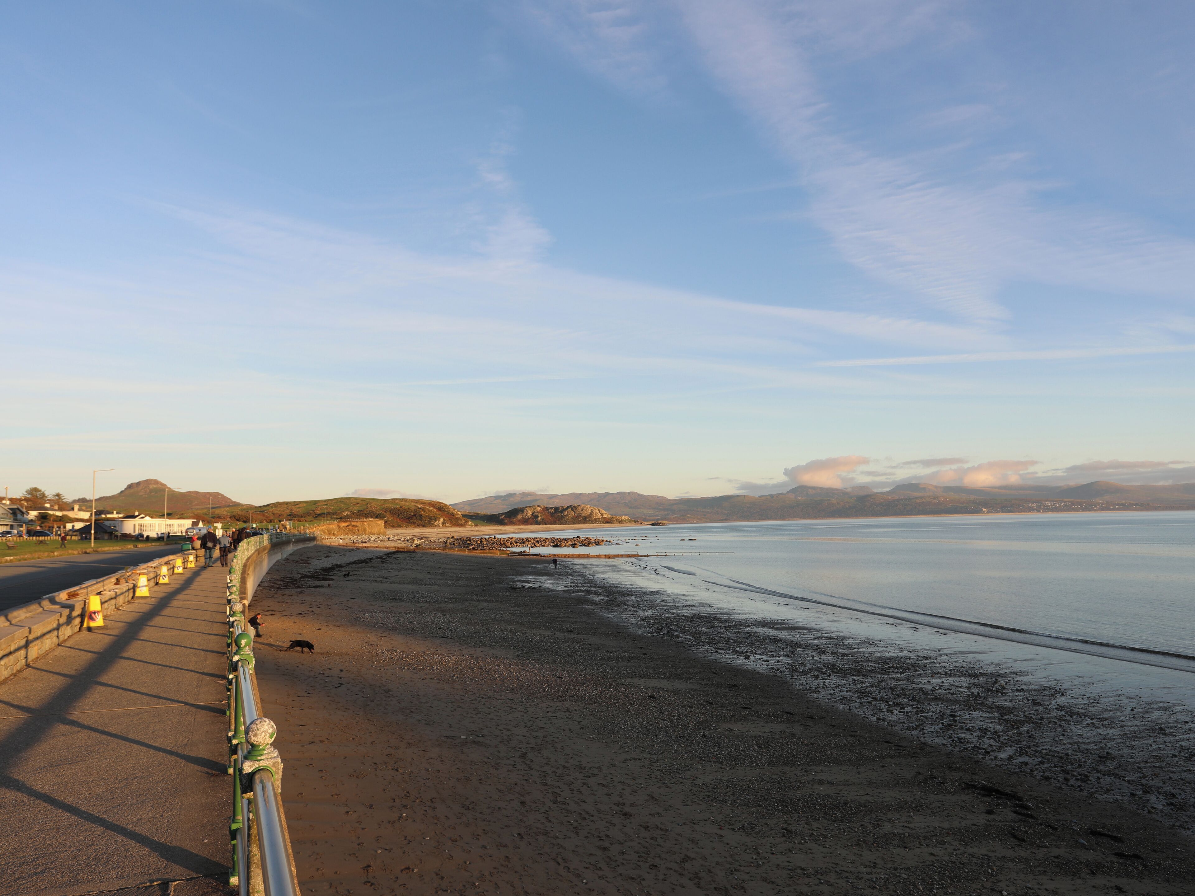 Une route côtière bordée d’une barrière de sécurité, une plage et des montagnes à l’horizon.