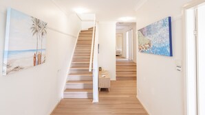 Um corredor com piso de madeira, escada e duas pinturas nas paredes.