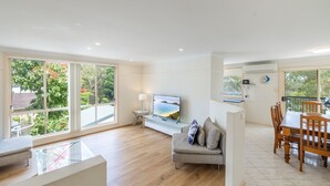 Uma sala de estar ampla com uma televisão grande, um sofá e uma área de jantar com mesa e cadeiras.