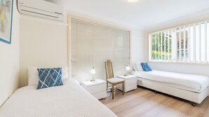 A modern bedroom with two beds, a nightstand, a chair, and a window with blinds. - Sea Breeze, 1,23 Stubby St Nelson Bay - Pet Friendly duplex with boat parking, air con and wi-fi (Nelson Bay)