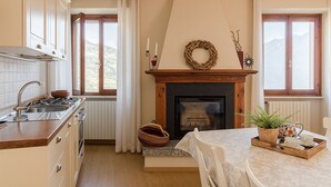 A cozy kitchen with a fireplace, wooden cabinets, and a dining area with a table set for two. - Corte Trepée, in the old town of Piovere (Tignale)