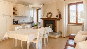 A cozy kitchen with a dining table, chairs, a fireplace, and a view of the outdoors. - Corte Trepée, in the old town of Piovere (Tignale)
