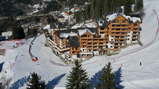 A large ski resort building with multiple balconies and a ski slope in the foreground. - "Loft Alpin" dans la Résidence l'Orée des Pistes (Oz)