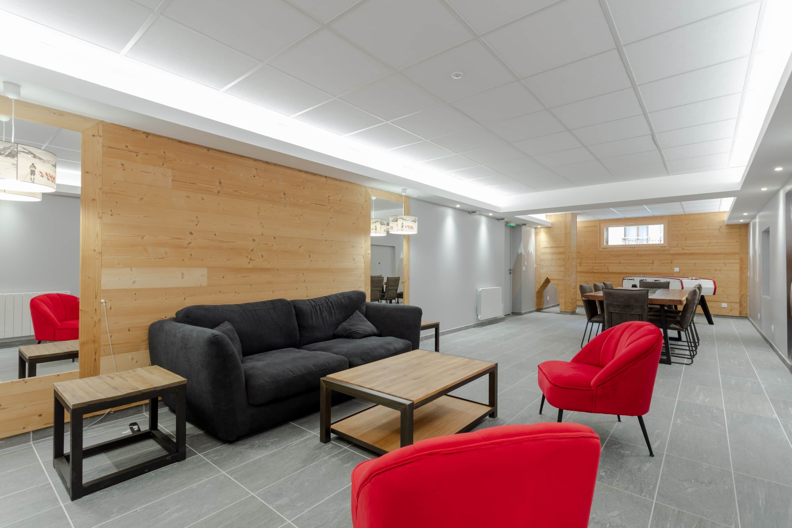 Een modern interieur met een houten wand, een zwarte bank, rode stoelen en een eethoek.