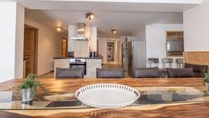 A modern kitchen with a built-in oven and a dining area with a glass table and grey sofas. - "Loft Alpin" dans la Résidence l'Orée des Pistes (Oz)