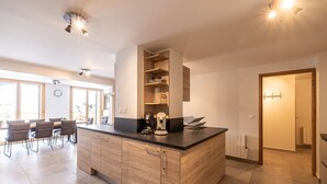 A modern kitchen with a central island, wooden cabinets, and a dining area with chairs and a table. - "Loft Alpin" dans la Résidence l'Orée des Pistes (Oz)