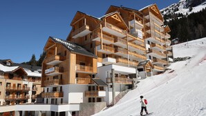 A multi-story wooden building with balconies, likely a hotel, situated on a snowy slope with a clear sky. - "Loft Alpin" dans la Résidence l'Orée des Pistes (Oz)
