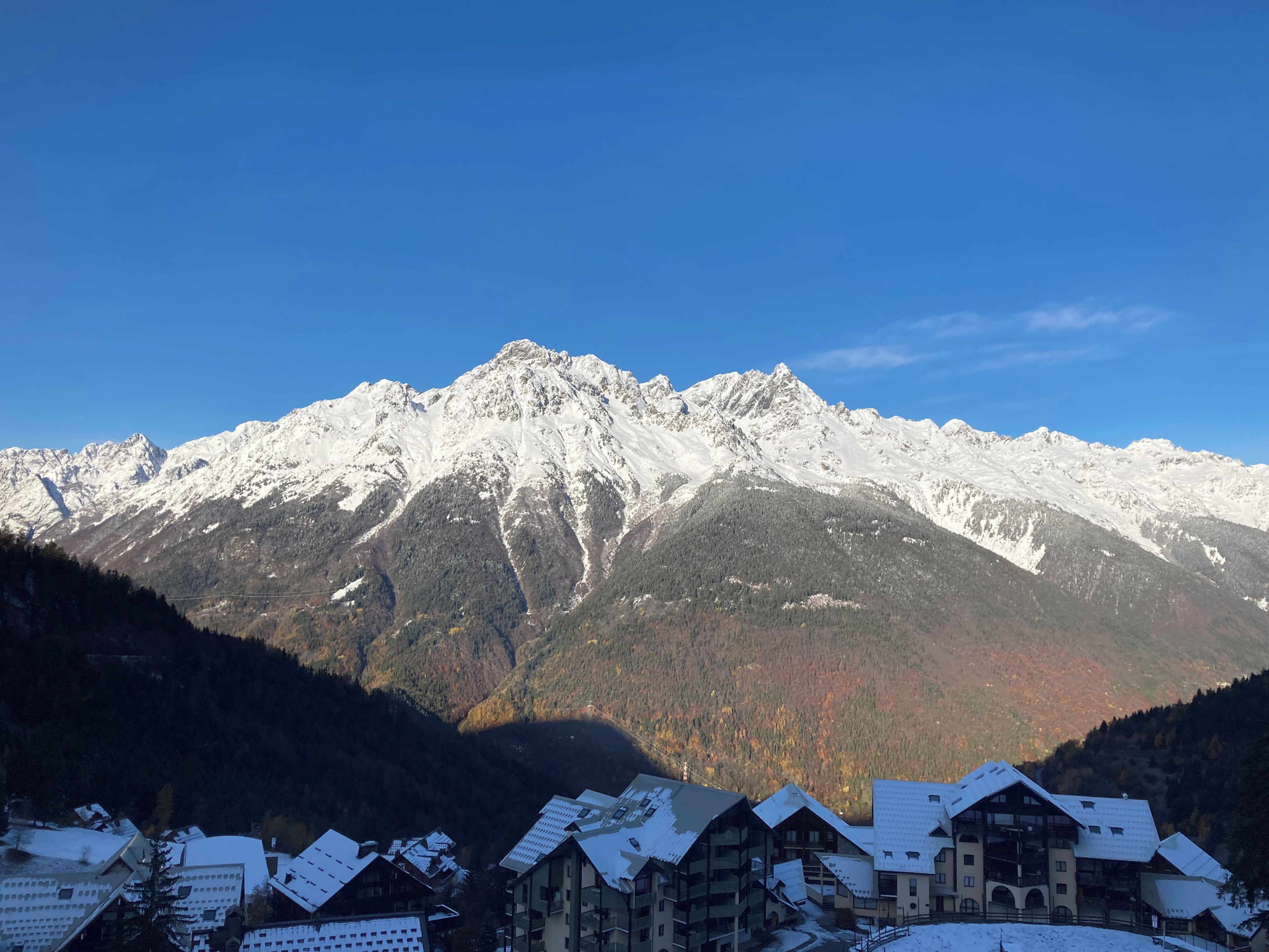 A mountain range with snow-covered peaks and a cluster of buildings with sloped roofs in the foreground.