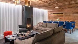 A modern living room with a fireplace, a dining area with blue chairs, and a wooden ceiling. - "Refuge des Sens", Chalet "Quiétude" (Vaujany)