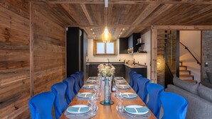 A wooden-paneled dining room with a long table set for six, blue chairs, and a chandelier. - "Refuge des Sens", Chalet "Quiétude" (Vaujany)