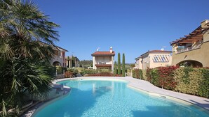 Una piscina cristalina rodeada de palmeras y setos cuidados, con edificios al fondo.