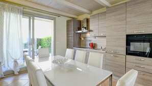 Una cocina moderna con armarios blancos, una mesa de comedor con sillas y un ventanal con cortinas.