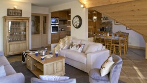Ein großzügiger Wohnbereich mit Sofa, Sessel, Esstisch aus Holz und einer Küche im Hintergrund.