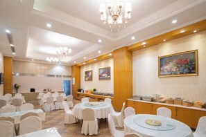 A banquet hall with round tables and chairs, a buffet area, and a painting on the wall.