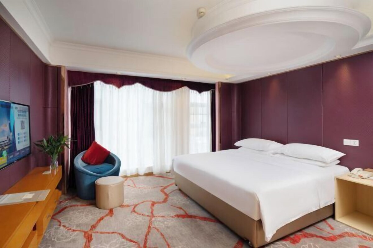 A hotel room with a large bed, a desk, a chair, and a small table.