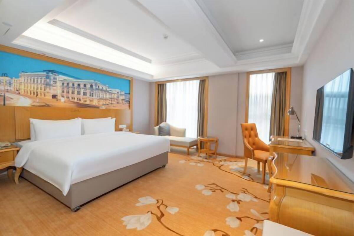 Habitación de hotel con una cama grande, un escritorio, una silla, un televisor y un cuadro en la pared.