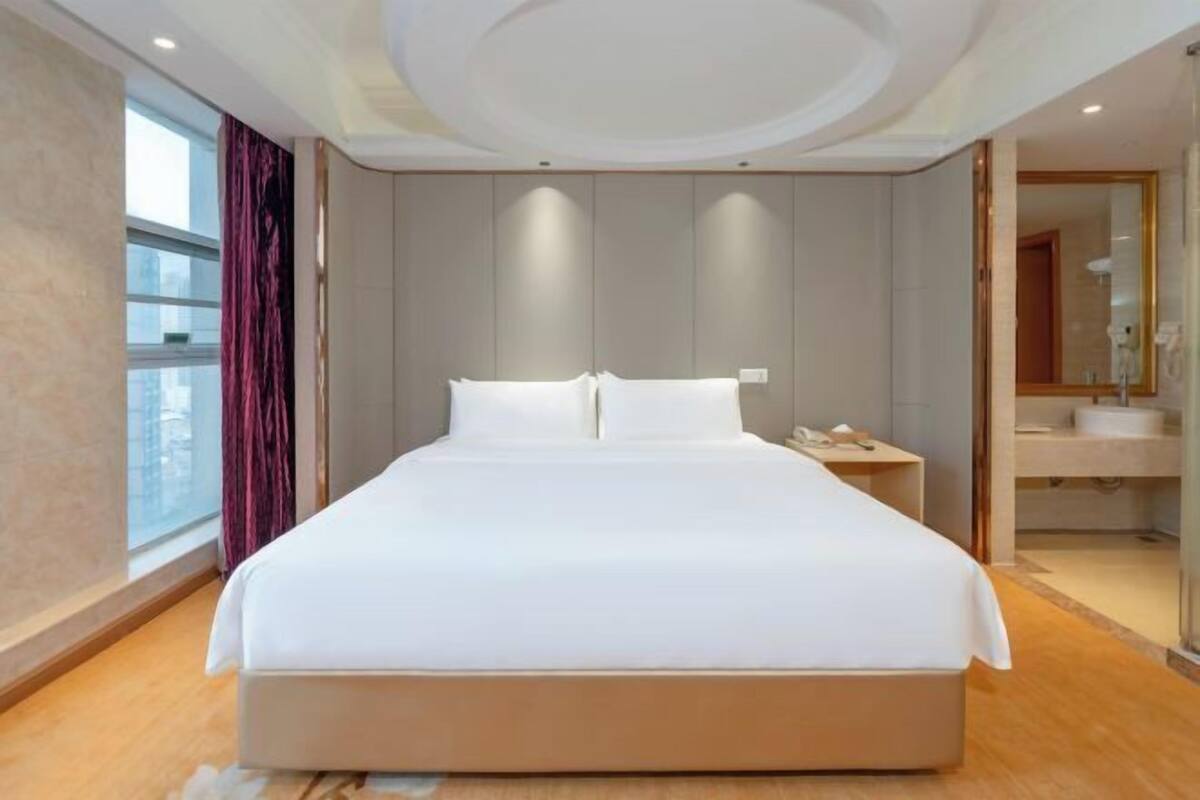 Una habitación de hotel moderna con una cama grande, una mesita de noche, un espejo y vistas a la ciudad.