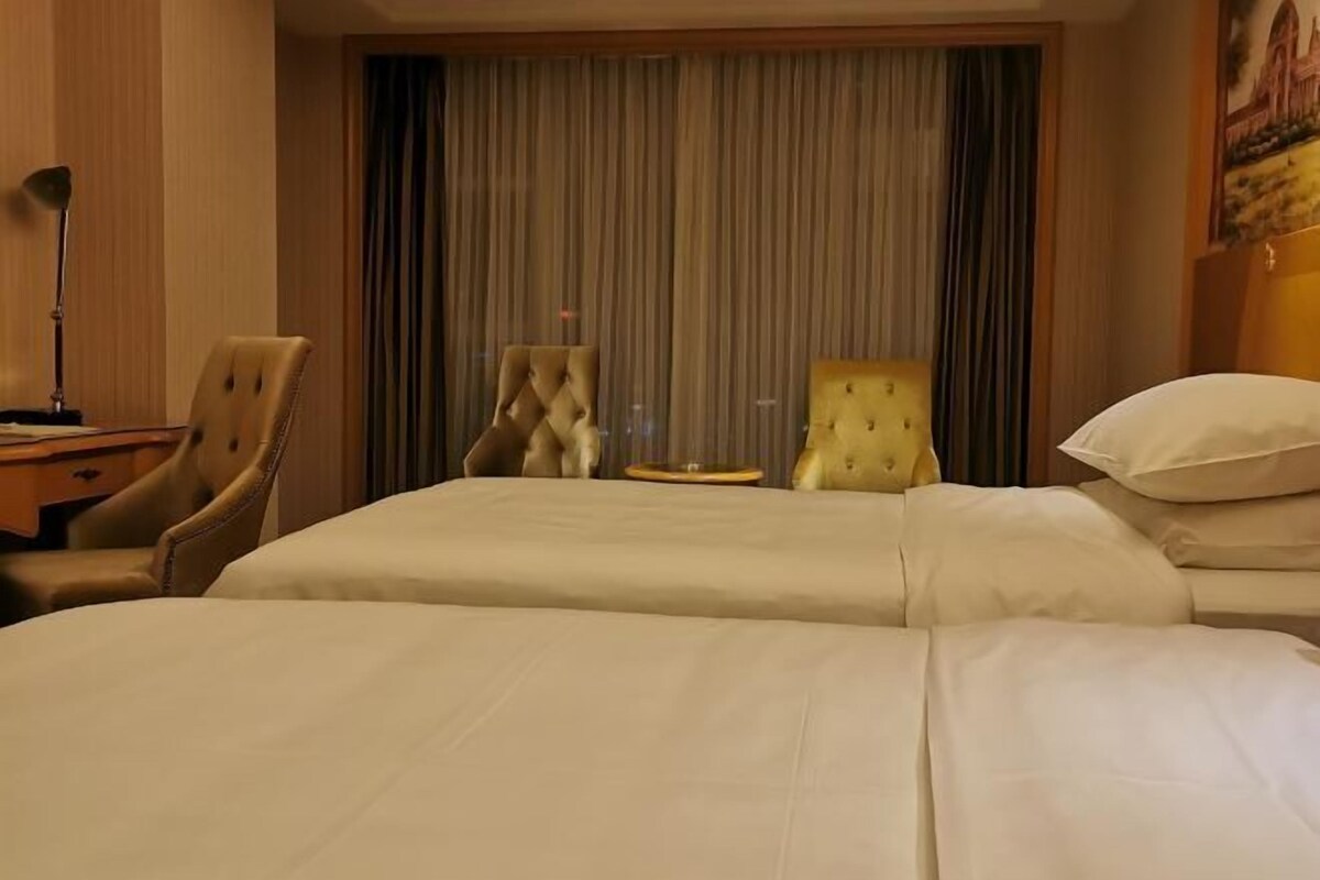 A hotel room with two beds, a desk with a lamp, and a chair.