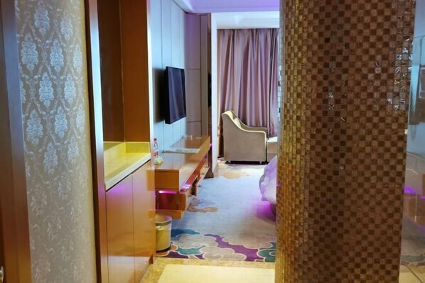 A hotel room with a bed, a TV mounted on the wall, a small seating area, and a patterned carpet. - Vienna International Hotel (Tianmen Wanda Plaza Donghu Branch) (Tianmen)