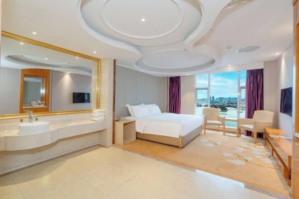 Habitación de hotel con una cama grande, un tocador con espejo, un sofá y vistas a la ciudad.