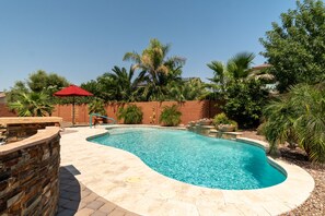 A swimming pool with a stone deck, surrounded by palm trees and a brick wall.
