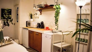 Une cuisine compacte avec des appareils électroménagers blancs, un four à micro-ondes, une machine à café et une étagère ornée de plantes vertes.