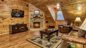 A log cabin interior with a fireplace, leather furniture, a television, and a ceiling fan. - Papa Bear, Hot Tub, WIFI,  $560 FREE tickets each paid day!!! (Sevierville)