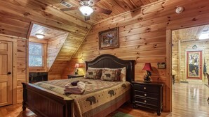 A cozy bedroom with a sloped ceiling, wooden walls, a bed with a quilt, a nightstand, a lamp, and a dresser. - Papa Bear, Hot Tub, WIFI,  $560 FREE tickets each paid day!!! (Sevierville)