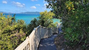 Un sentier pavé, bordé d’une rambarde en bois et entouré de verdure, mène à un point de vue sur la côte.