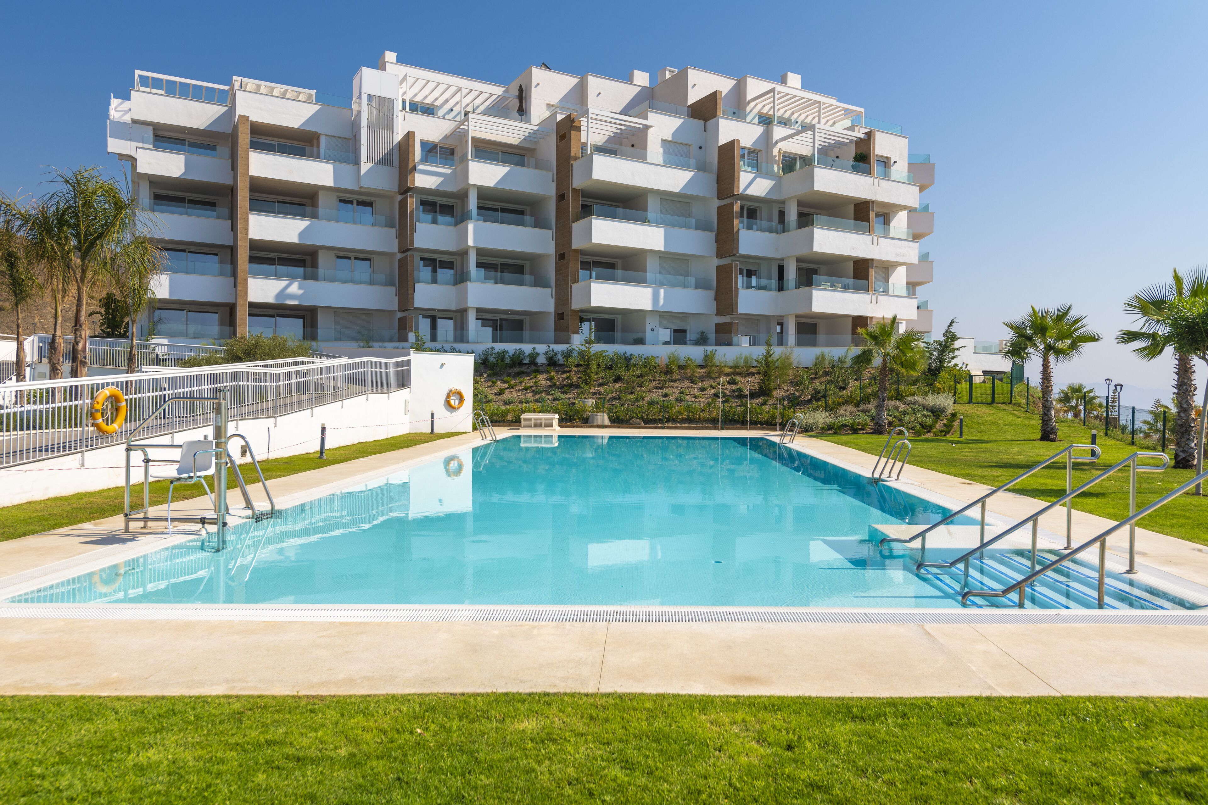 A modern multi-story hotel with a swimming pool, surrounded by palm trees and a well-maintained lawn.