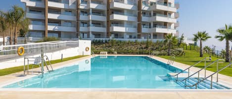 A modern multi-story hotel with a swimming pool, surrounded by palm trees and a well-maintained lawn.