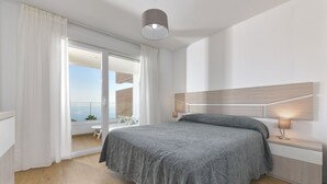 A modern bedroom with a large bed, a nightstand with a lamp, and a sliding glass door leading to a balcony.
