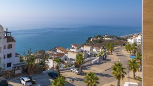 A coastal residential area with white buildings, palm trees, and a view of the sea.