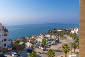 A coastal residential area with white buildings, palm trees, and a view of the sea.