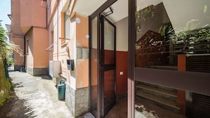 Entrada de un edificio con puerta de cristal, una bicicleta estacionada afuera y un contenedor de basura.