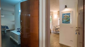 Un pasillo con puerta de madera, un radiador, una mesa con sillas y un cuadro en la pared.