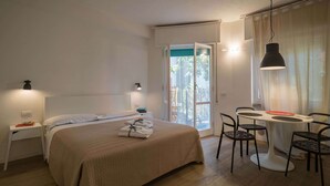 Una habitación de hotel con cama, mesitas de noche, un escritorio con sillas y una ventana con cortinas.