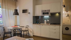 Cocina compacta equipada con microondas, horno y lavadora. Cuenta con un pequeño comedor con mesa y sillas.