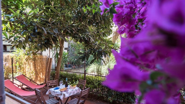 Un patio exterior con una mesa dispuesta para comer, rodeado de follaje y una cerca.