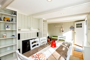 A room with a wooden table, white chairs, a fireplace, and shelves with various items.