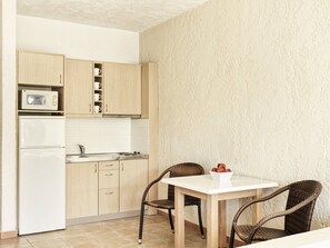 Eine kleine Küche mit Holzschränken, einem weißen Kühlschrank, einer Mikrowelle und einem Esstisch mit Korbstühlen.