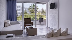 Una habitación de hotel moderna con sofá, sillón y una pequeña mesa con un libro. Cuenta con un balcón con una silla y un televisor montado en la pared.