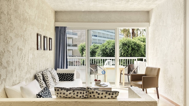 Una sala de estar moderna con sofá, sillas, una mesa de centro y un balcón con vistas a zonas verdes y edificios.