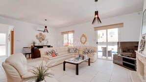A spacious living room with a sofa, coffee table, and a TV stand. There is a dining area with a table and chairs, and a kitchen in the background. - Villa Hanna  3 Bedrooms (Protaras)