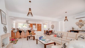 A spacious living room with a sofa, coffee table, and a fireplace. There is a kitchen area with a dining table and chairs. - Villa Hanna  3 Bedrooms (Protaras)