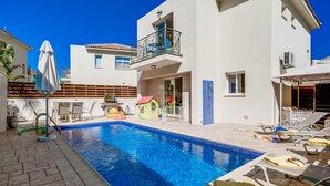 A swimming pool with lounge chairs and a small playhouse.